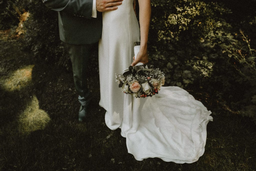 gros plan sur le bas d'une robe de mariée avec un bouquet